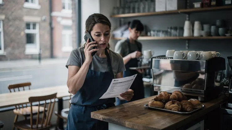 A café owner on the phone at her counter, holding an energy bill