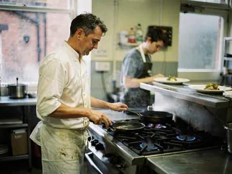 A chef cooking on lit gas hobs in a restaurant kitchen