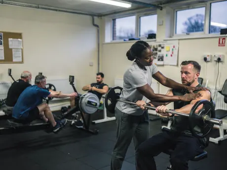 A coach helping a member with his technique in a community gym