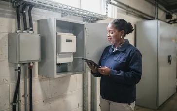 A facilities manager checks a half-hourly electricity meter in a factory plant room