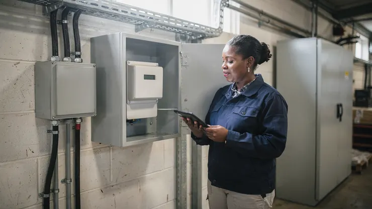 A facilities manager checks a half-hourly electricity meter in a factory plant room