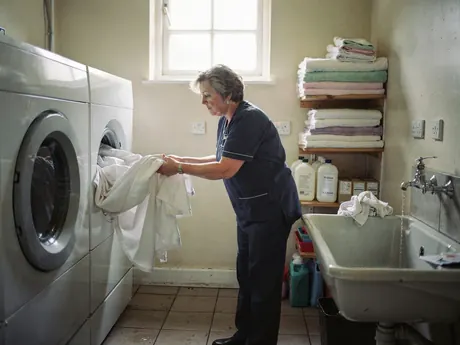 A housekeeper loading sheets into a washing machine in a hotel laundry