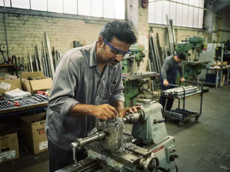 A machinist operating a lathe on a busy workshop floor