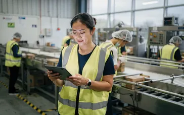 A production manager checking figures on a tablet on a factory floor