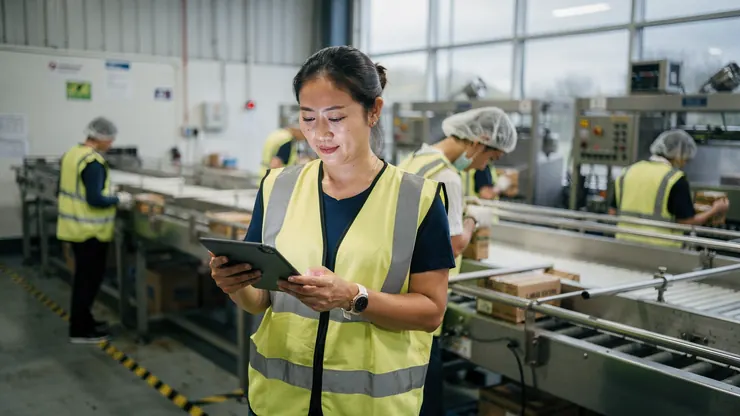 A production manager checking figures on a tablet on a factory floor