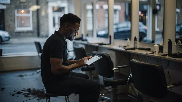 A salon owner checking a bill on a tablet in his empty salon after closing