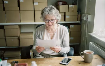 A shop owner reading a printed quote at her desk, with her phone beside it