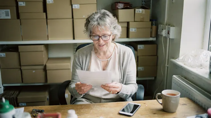 A shop owner reading a printed quote at her desk, with her phone beside it