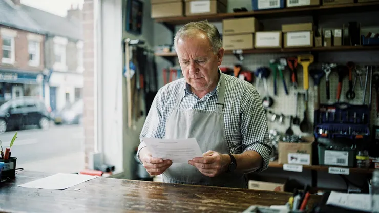 A shopkeeper reading a letter at the counter of his hardware shop